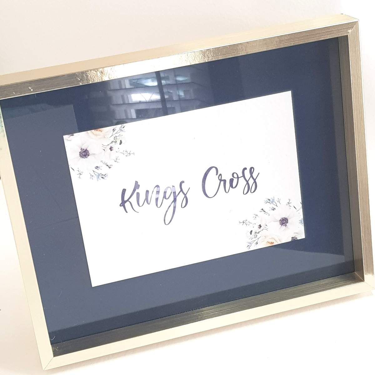 A navy and white wedding table name with floral design in a pale gold frame