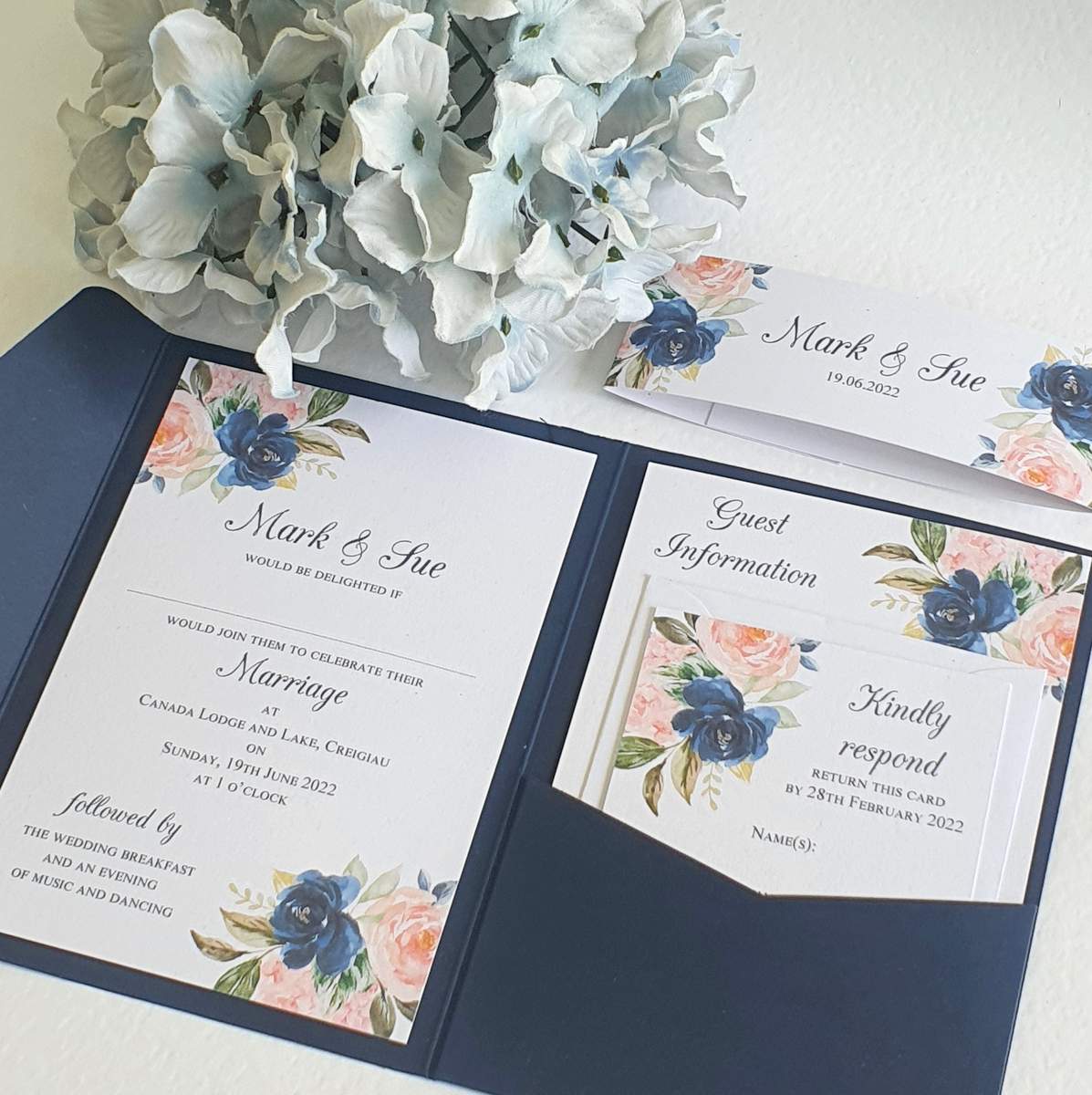 an open wedding invitation with inserts printed with a pretty navy and blush floral design