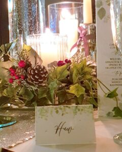 a wedding place card on a table dressed for a christmas wedding with candles, greenery and berries