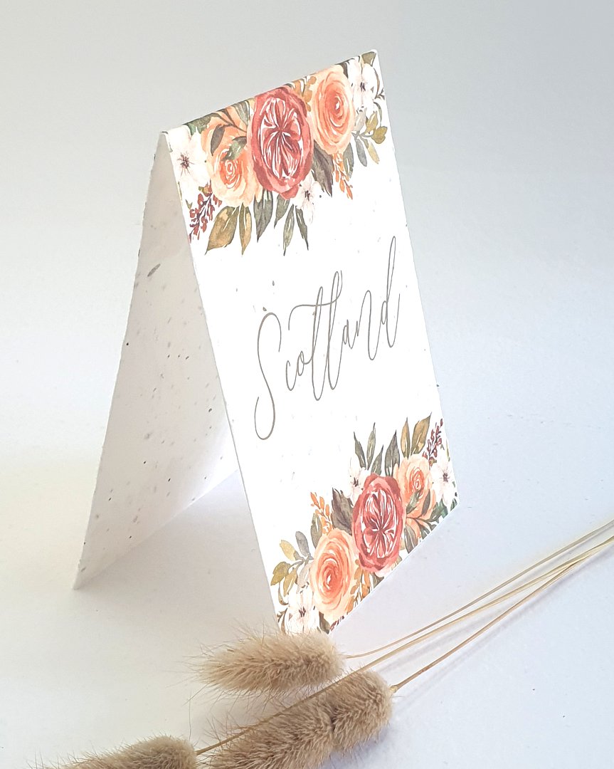 A wedding table name card with the word Scotland on, an autumnal floral design top and bottom. Sideways view to show how the tent style table name stands on its own
