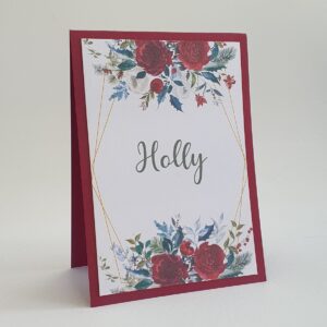 a festive theme wedding table name card, with a green and red floral design around the text