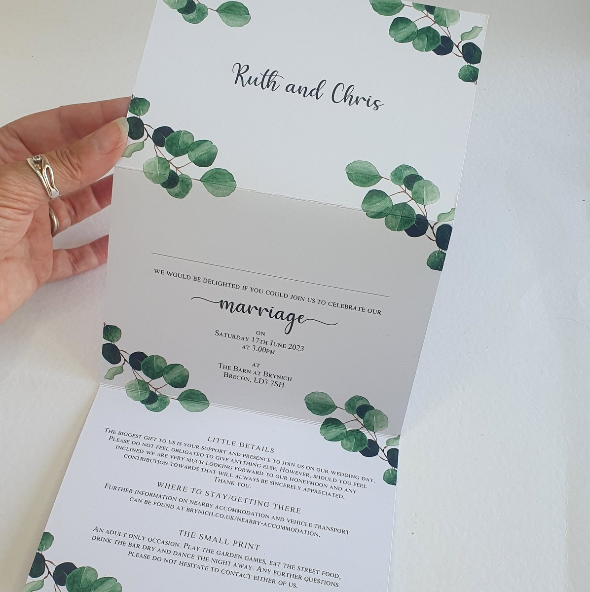 a concertina style wedding invitation with eucalyptus leaves on the corners