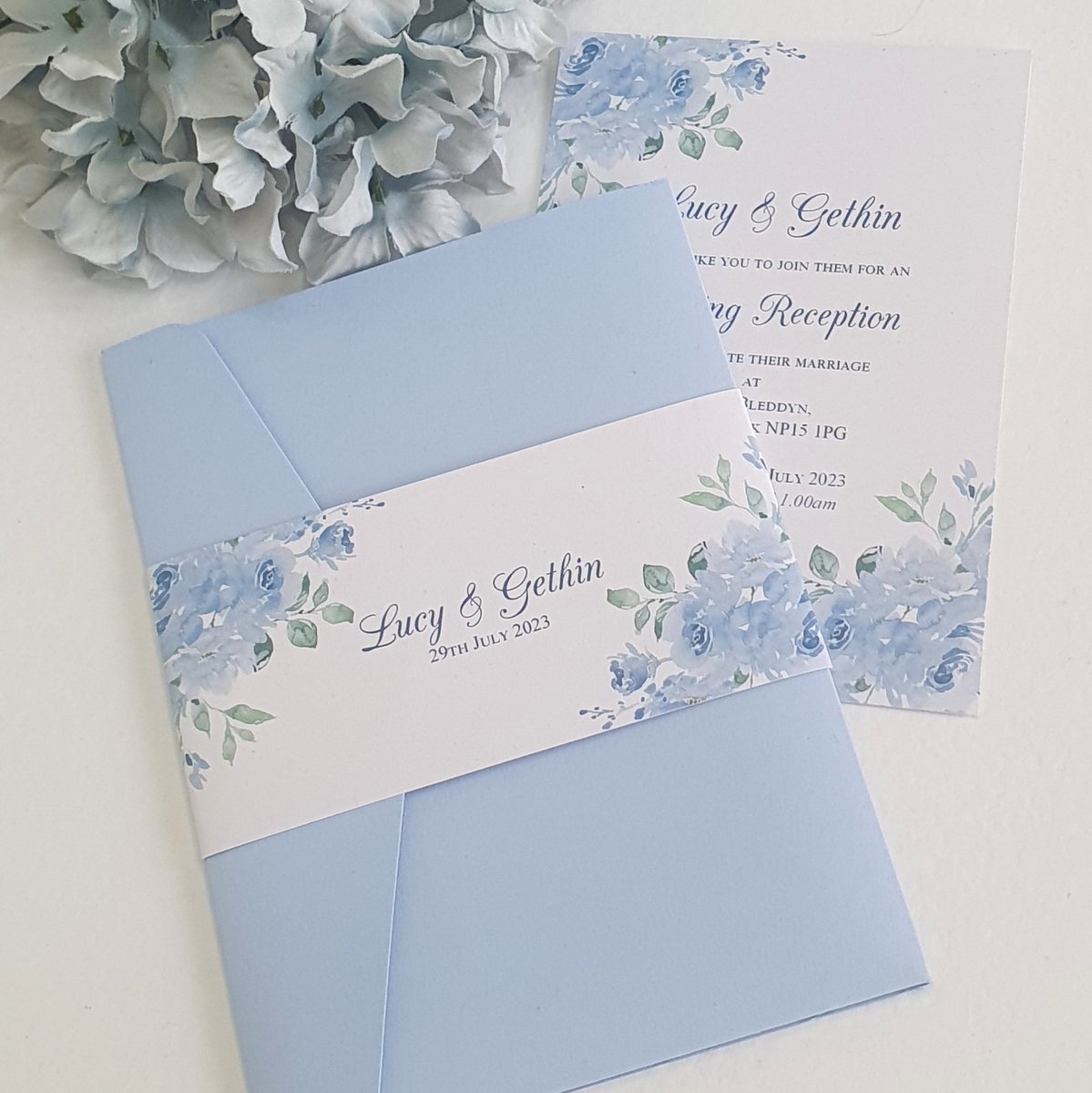 two wedding invitations with a sky blue floral design