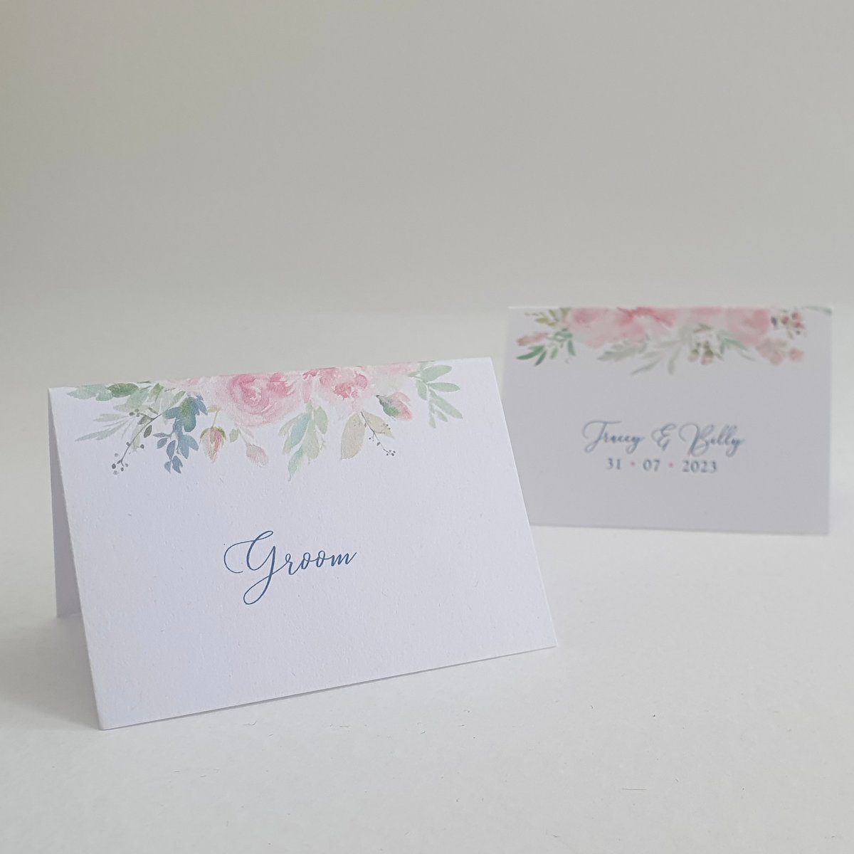 wedding place name cards, one shows the front with a pink floral design, the other shows the back with the bride and grooms names and wedding date