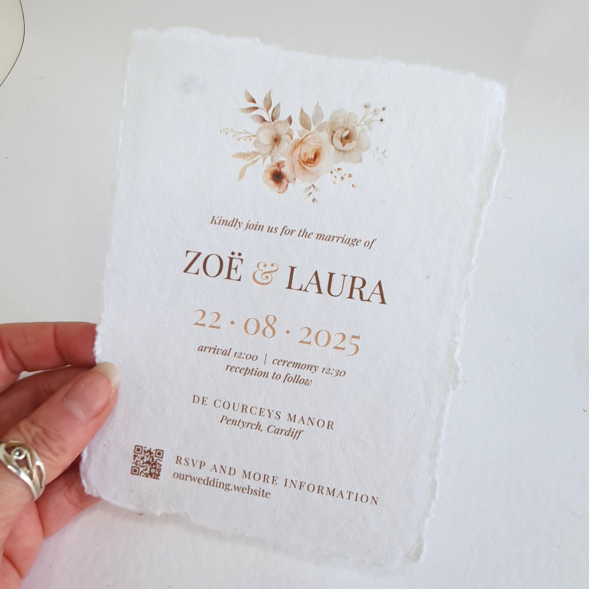 a wedding invitation printed on handmade paper with a torn deckle edge. There is a champagne floral bouquet design at the top above the text