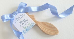 a personalsised wedding favour tag with a blur floral design, tied with blue ribbon onto a small wooden welsh love spook